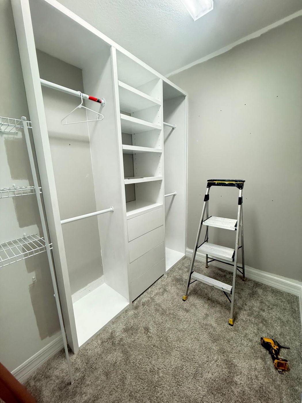 A closet system mid-install with a step ladder and drill on the floor